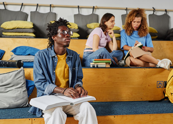 portrait of blind African American man reading book in braille while sitting in school stalls