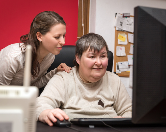 woman with learning disability on computer being helped by home carer