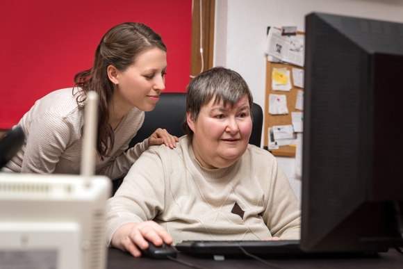 woman with learning disability on computer being helped by home carer
