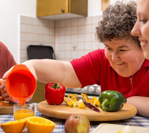 woman with learning disabilities prepping dinner with help from carer and pouring fresh fruit juice