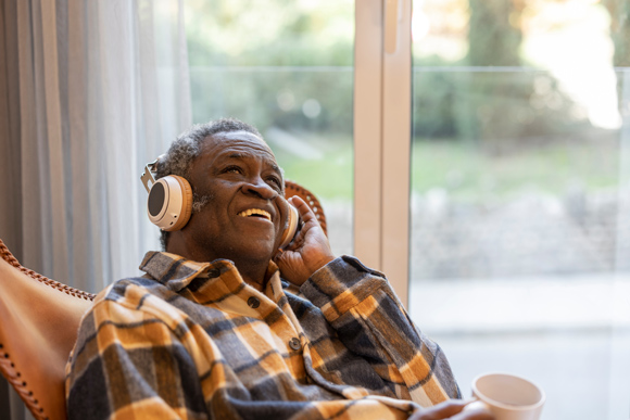 adult man listening to music via headphones smiling and sitting at home