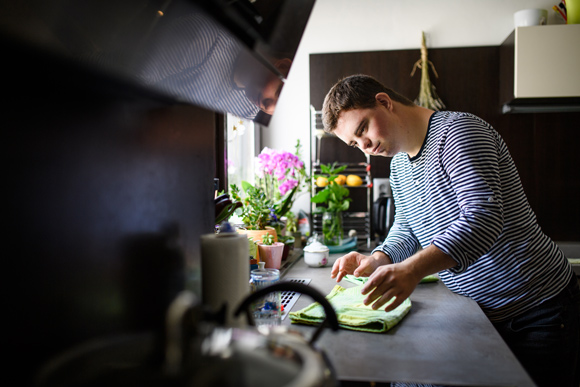Down syndrome adult man standing indoors in kitchen at home, cleaning